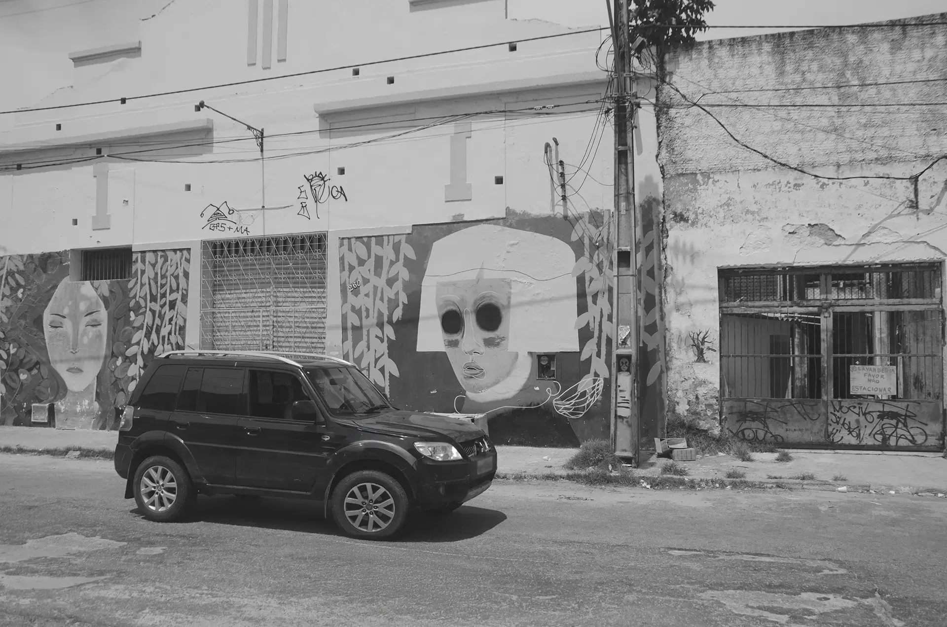 Frame 1 in grayscale of a sequence showing a car crossing a street in downtown Fortaleza from left to right with a graffiti mural in the background