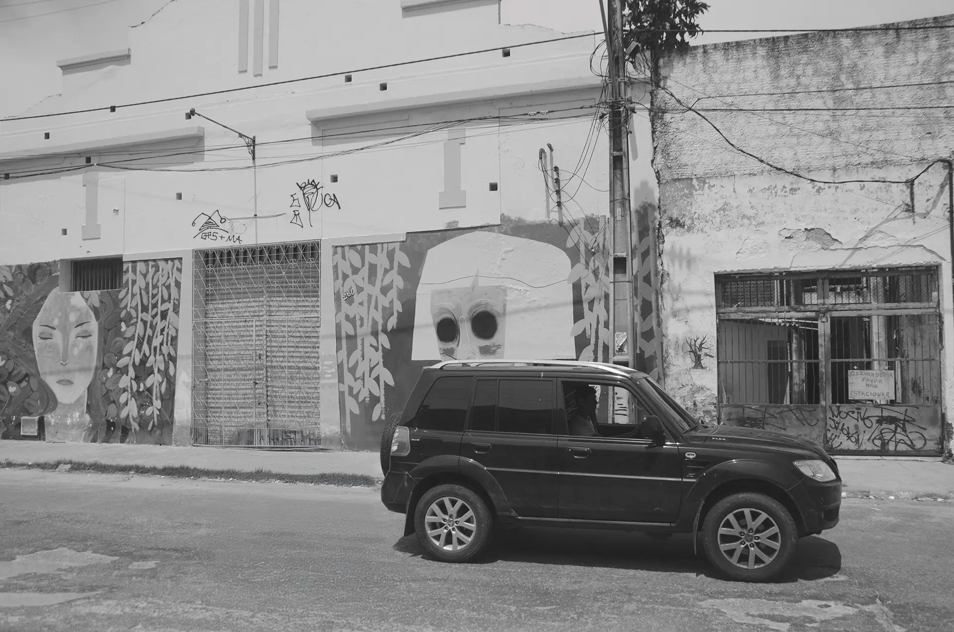 Frame 2 in grayscale of a sequence showing a car crossing a street in downtown Fortaleza from left to right with a graffiti mural in the background