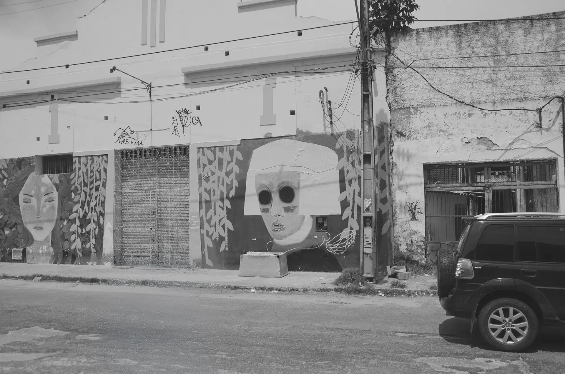 Frame 3 in grayscale of a sequence showing a car crossing a street in downtown Fortaleza from left to right with a graffiti mural in the background