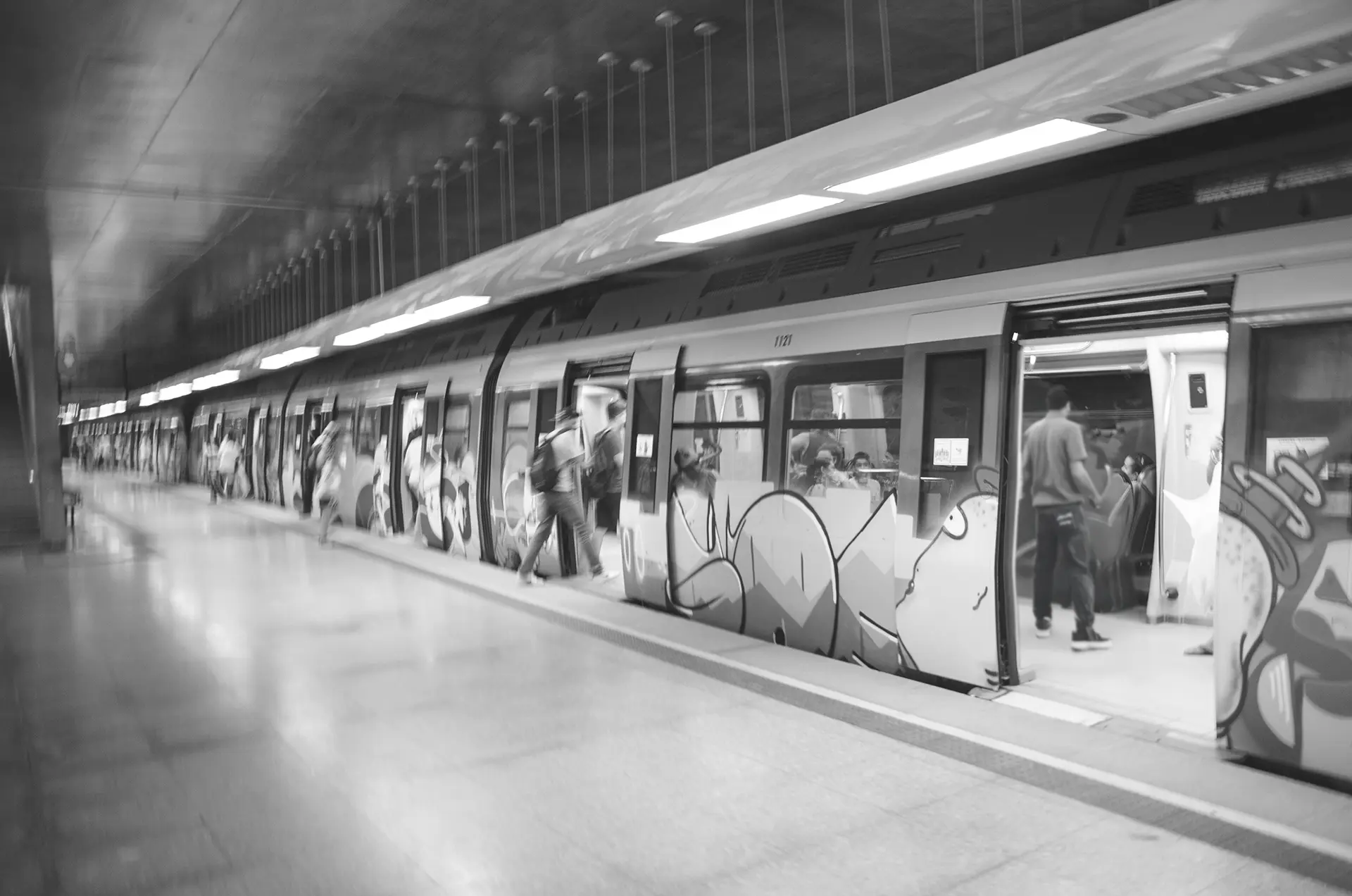 Grayscale photograph of the graffiti-covered train with open doors at Benfica Metro Station in Fortaleza as passengers enter and exit the train car