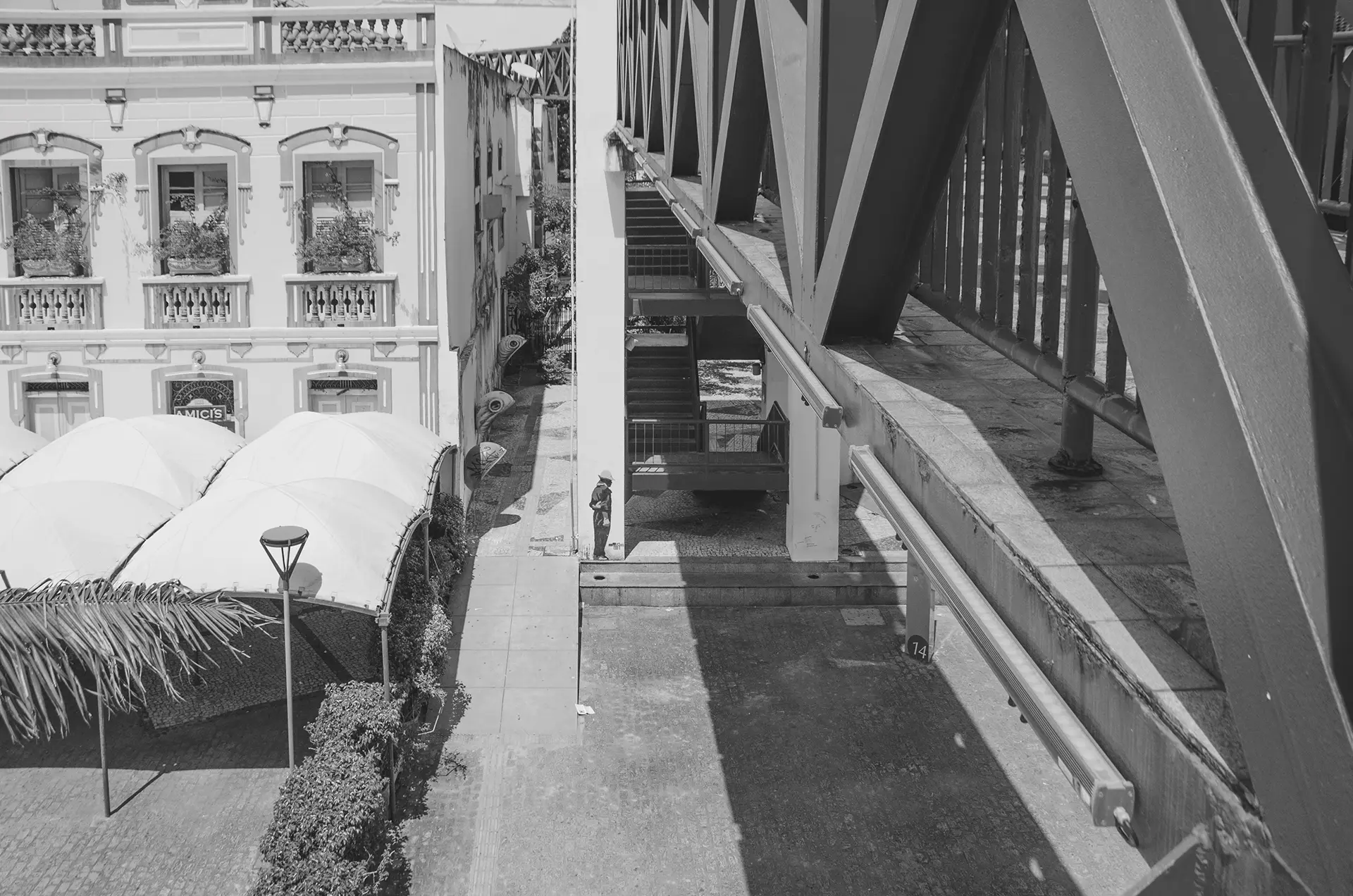Grayscale photograph in perspective of one of the walkways at the Dragão do Mar Cultural Center in Fortaleza, where you can see the silhouette of a man from behind with his arms crossed, made with a stencil on the column of the walkway