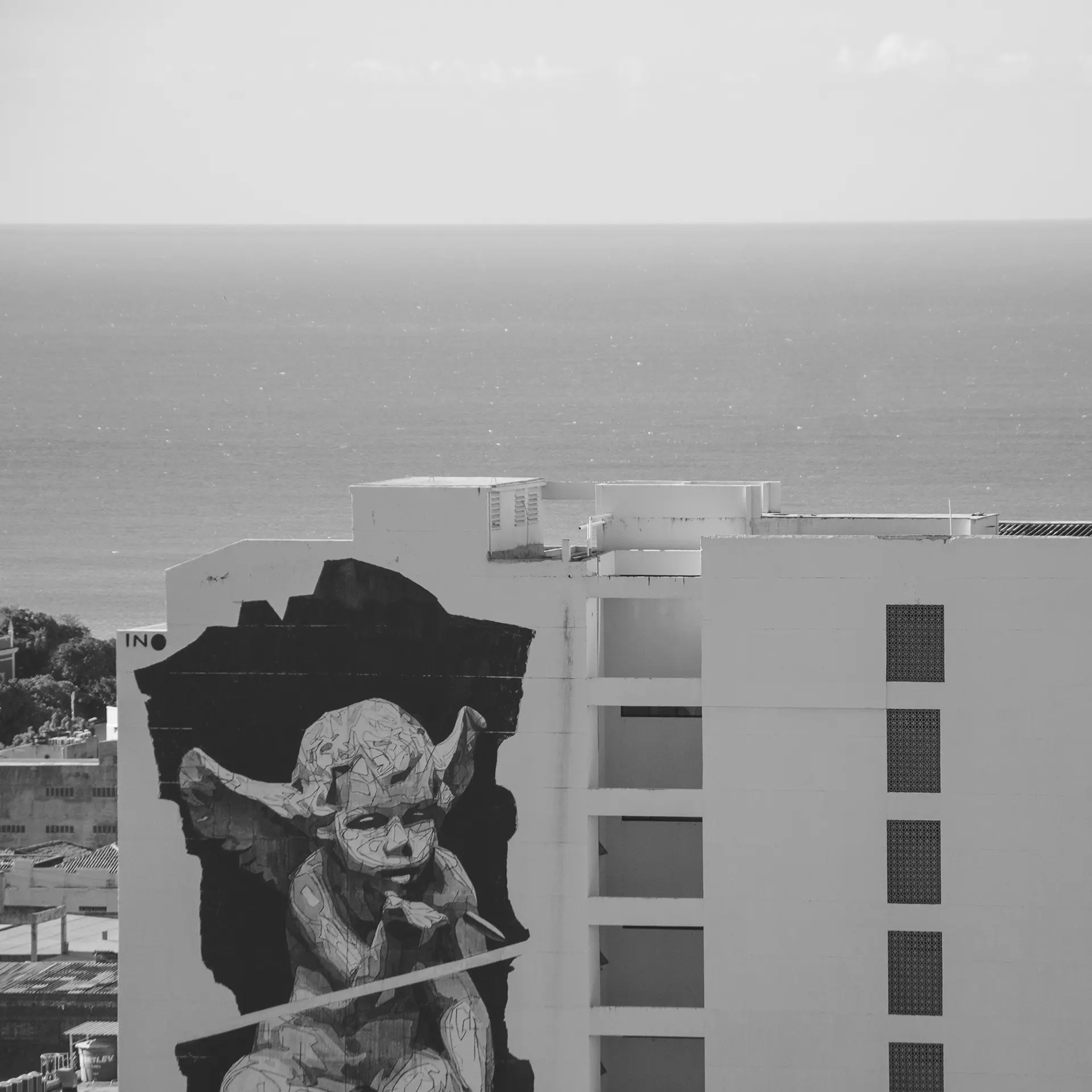 Grayscale photograph taken from the top of a building showing a giant mural on the side of a building with a little angel blowing a bubble in downtown Fortaleza