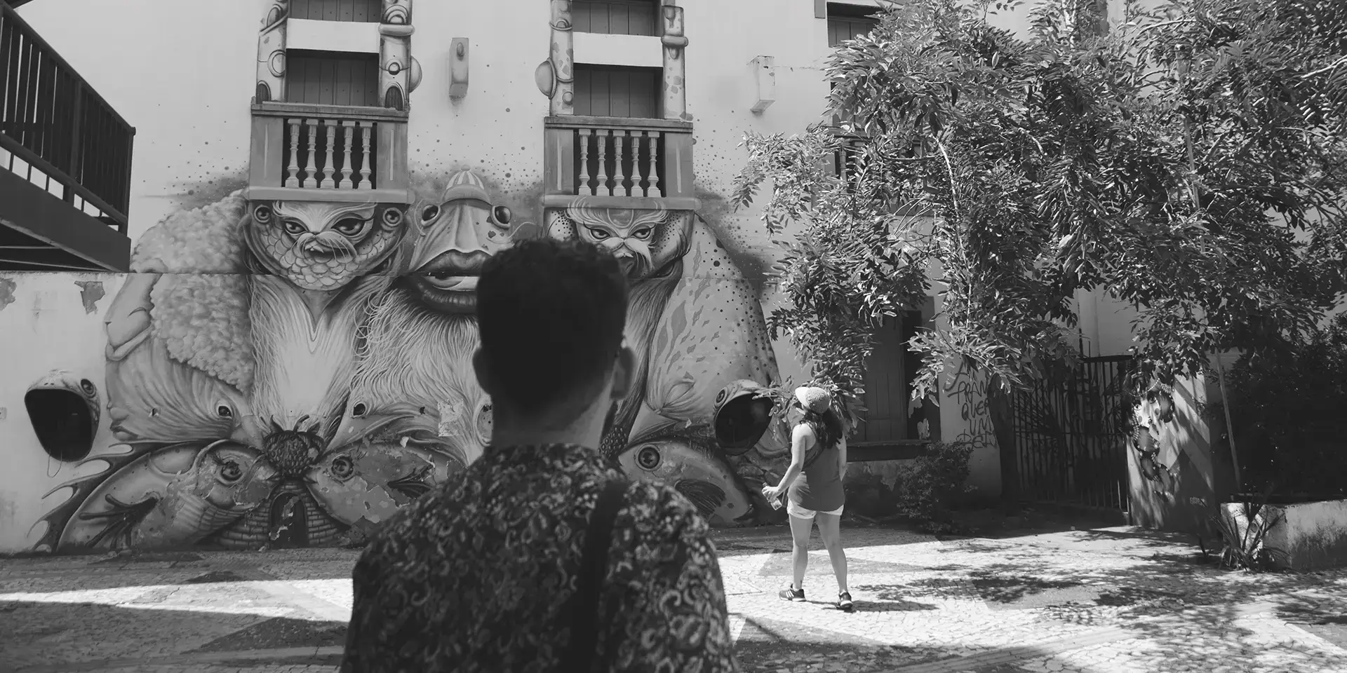 Grayscale photograph of a man from behind looking at a graffiti mural at the Dragão do Mar Cultural Center in Fortaleza