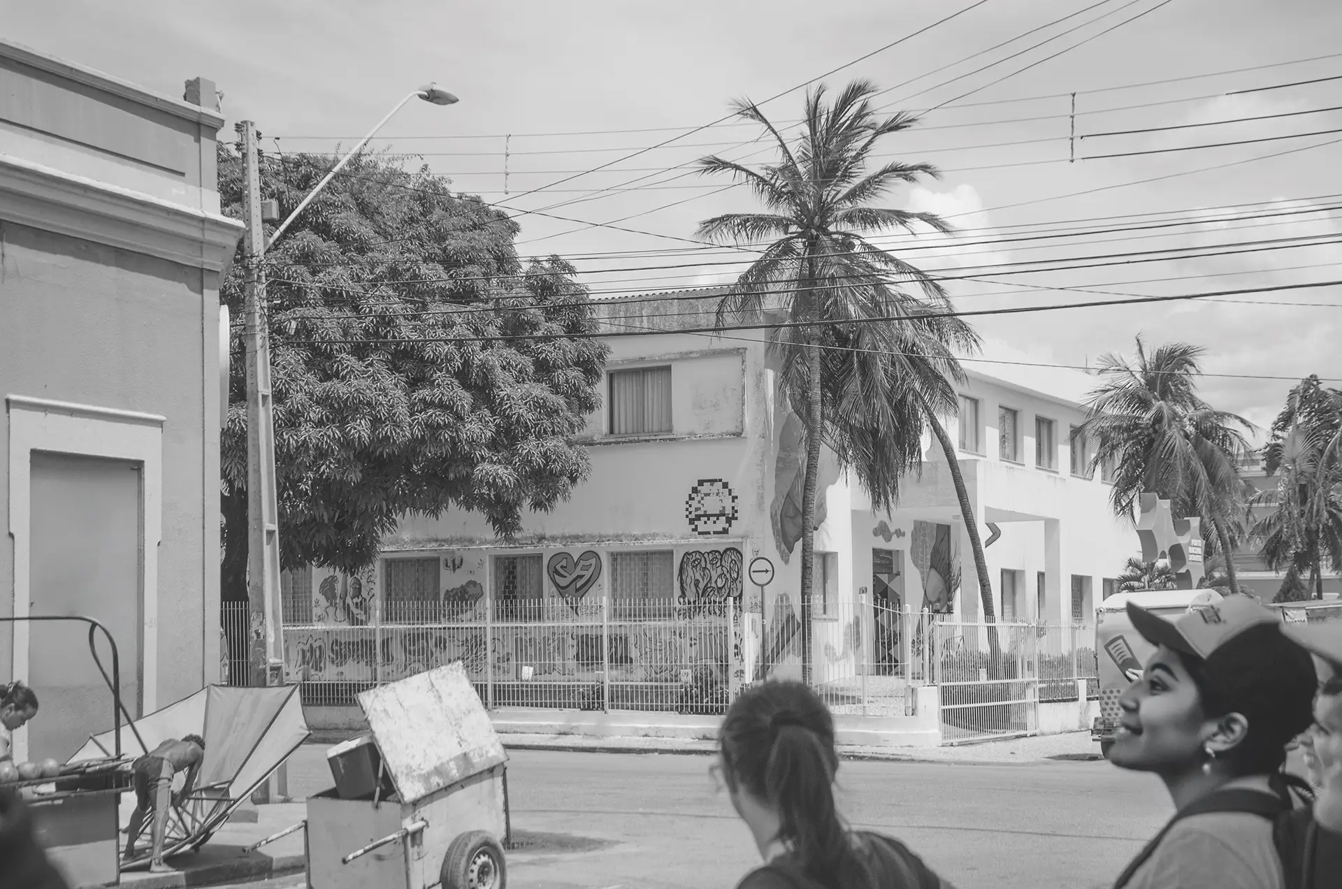 Grayscale photograph further away from a public building with several urban art interventions with a woman from behind observing the building