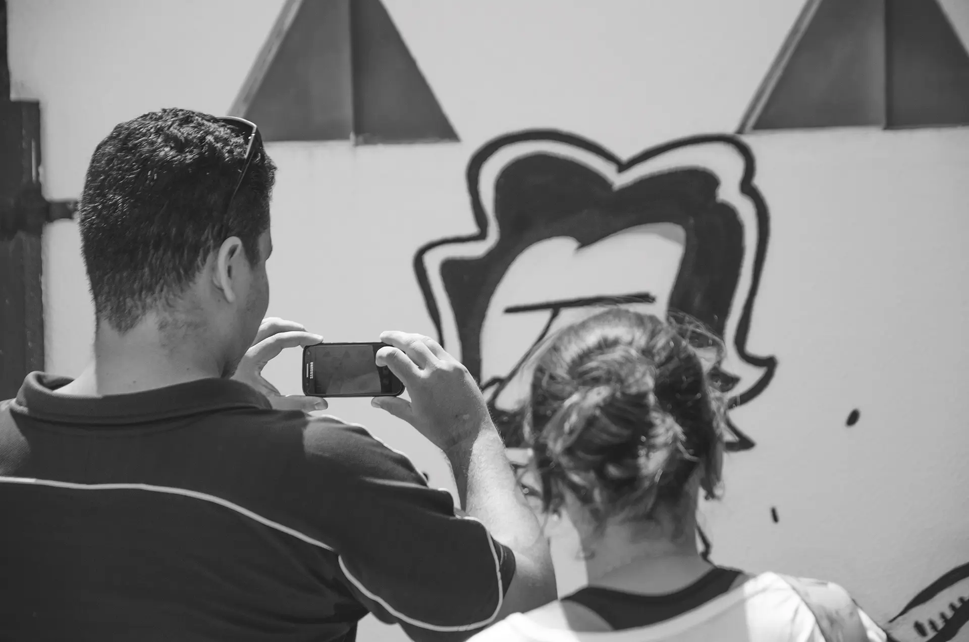 Grayscale photograph of people taking photos with their cell phones in front of a graffiti mural