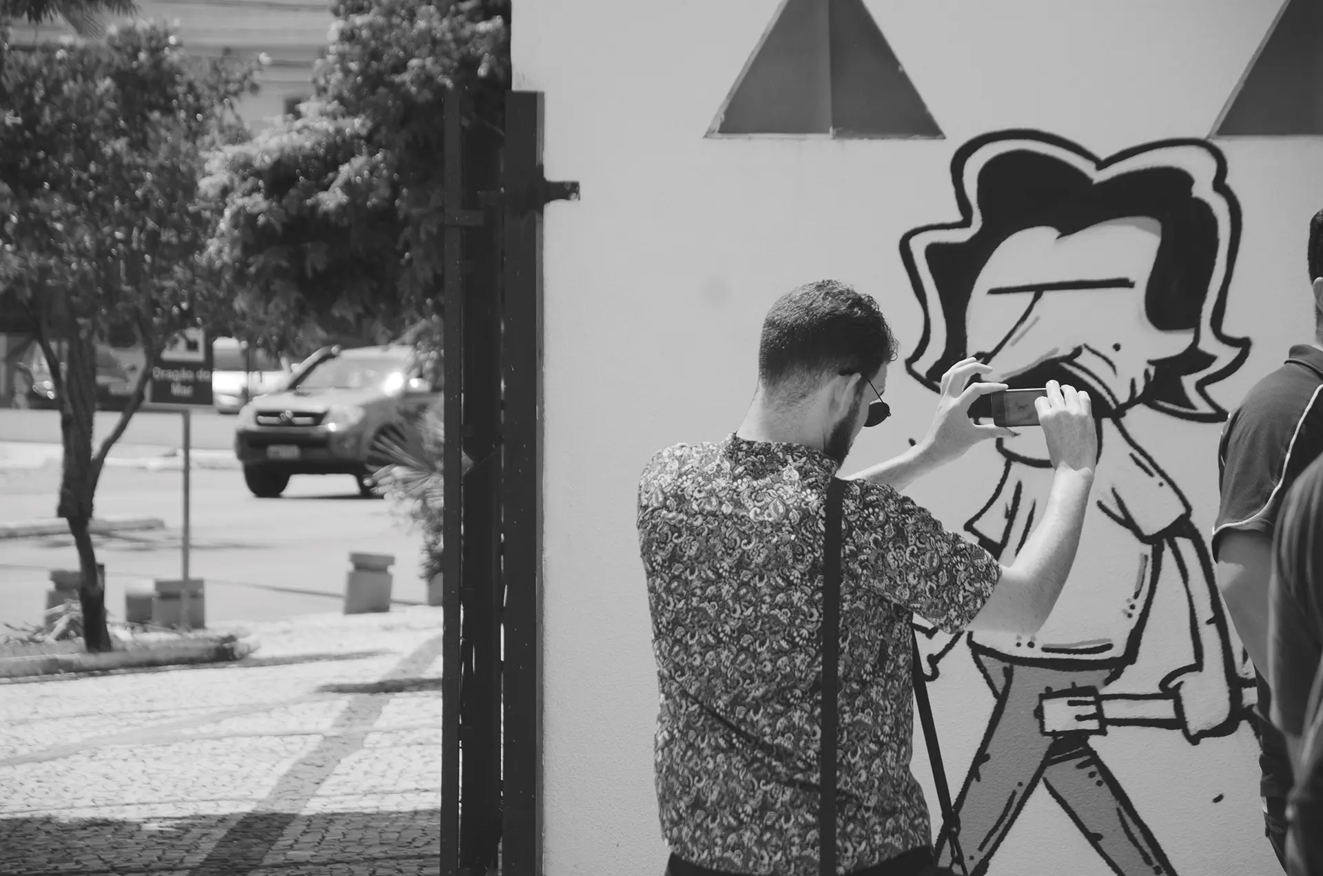 Grayscale photograph of people taking photos with their cell phones in front of a graffiti mural