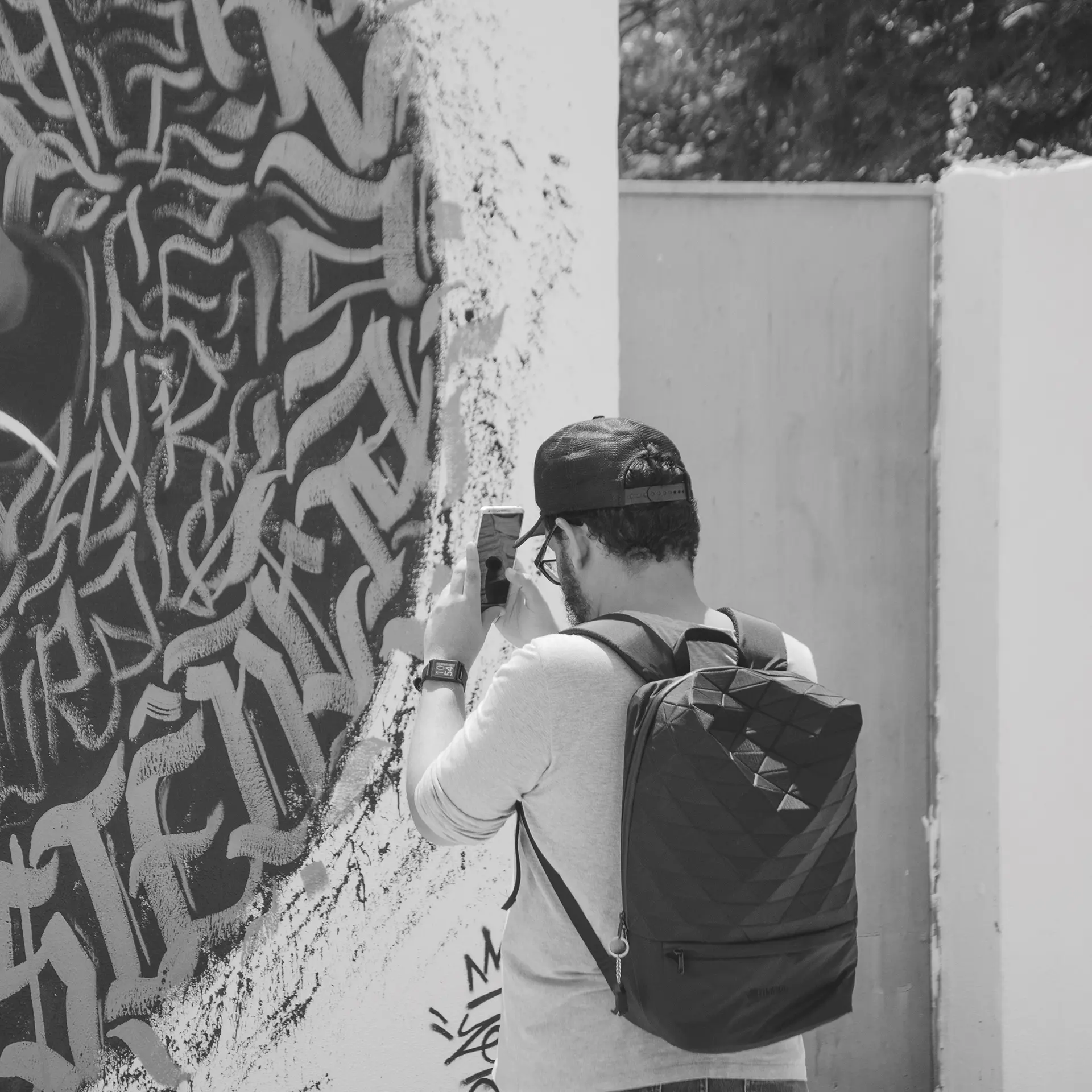 Grayscale photograph of people taking photos with their cell phones in front of a graffiti mural