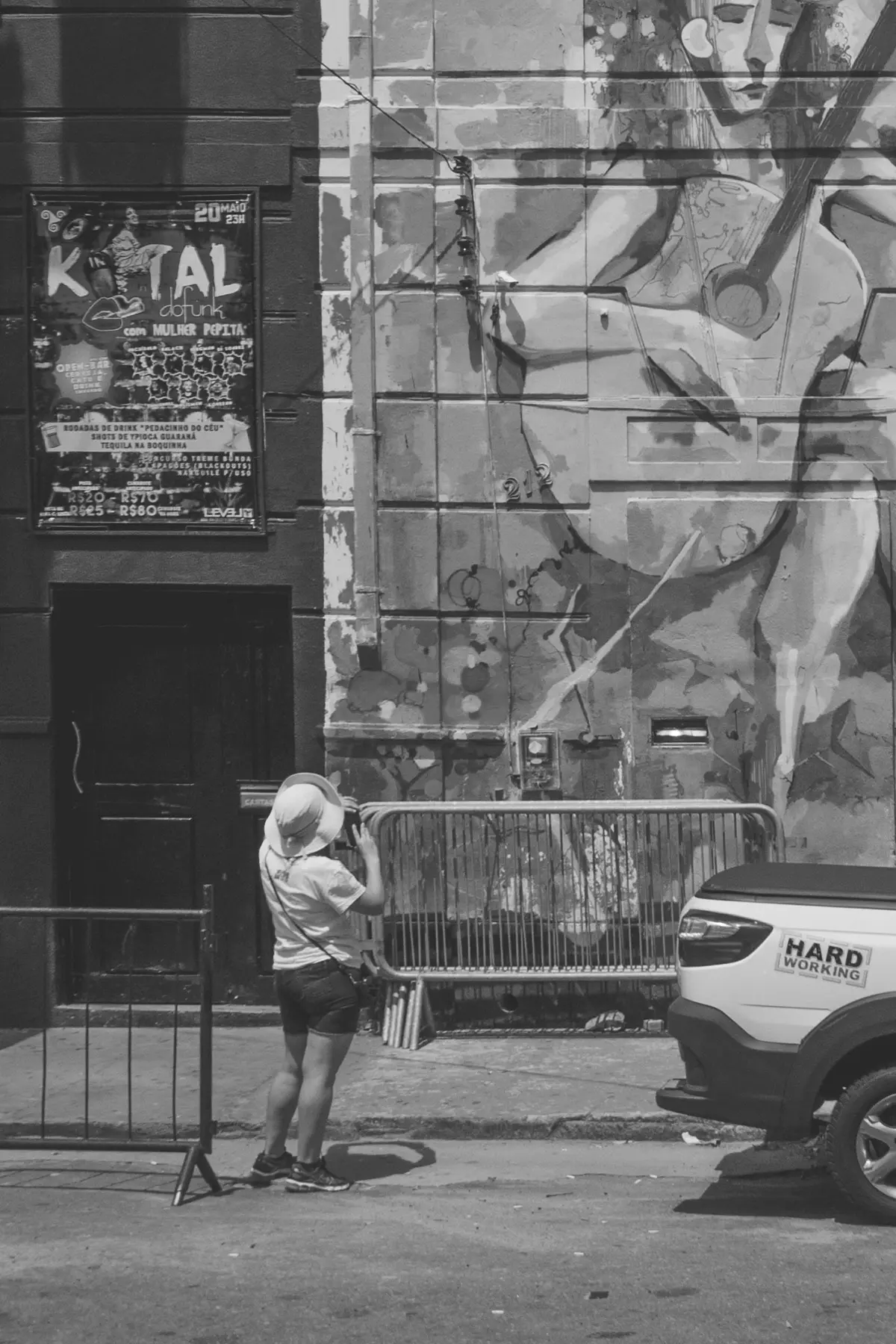Grayscale photograph of an old building completely covered in graffiti with a woman from behind holding a phone while photographing the mural