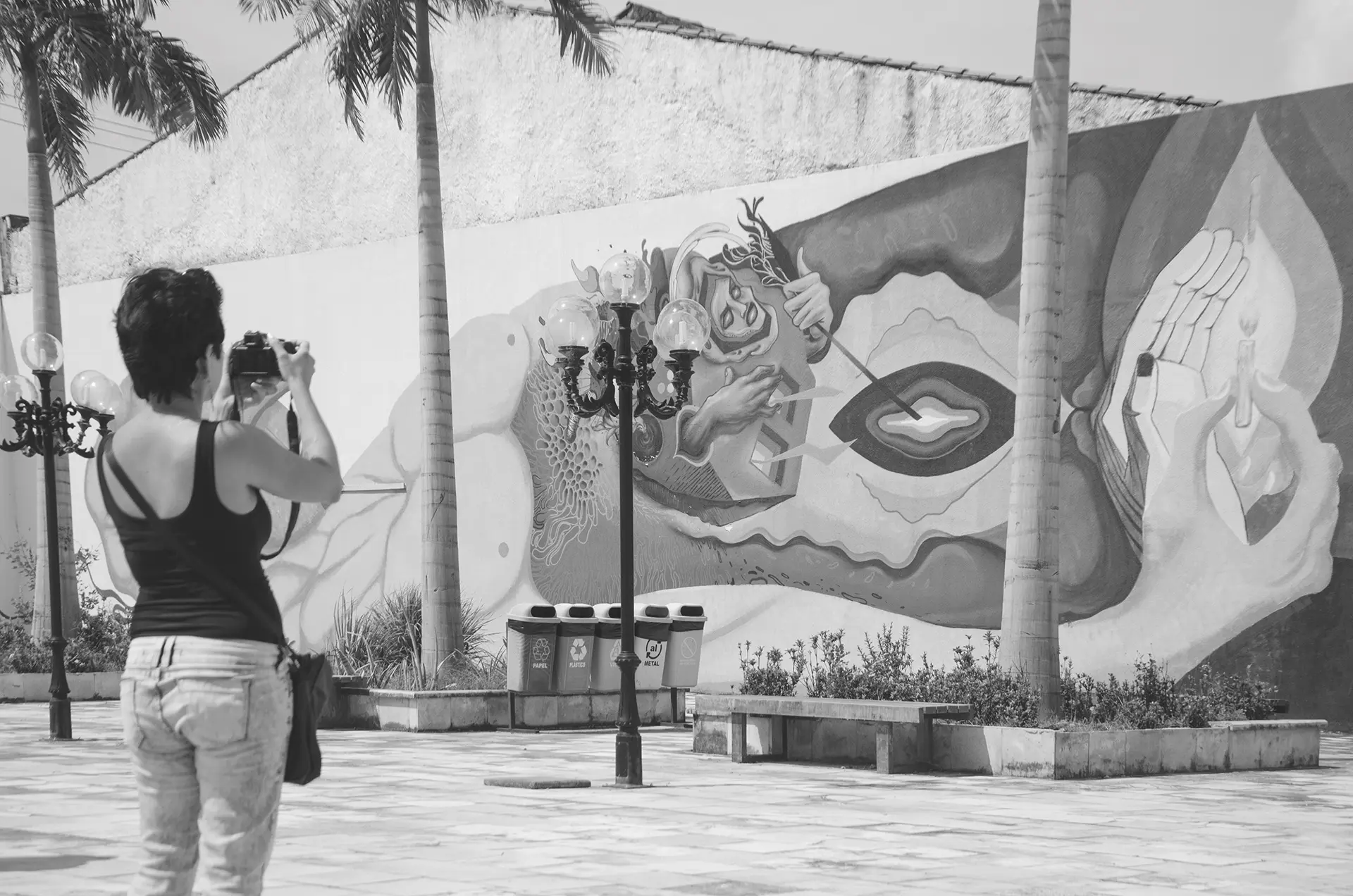 Grayscale photograph of a woman from behind photographing a graffiti mural on the wall of a square in downtown Fortaleza with a professional camera